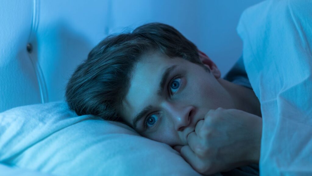 Homme allongé inquiet dans son lit, regardant fixement avec une expression effrayée.