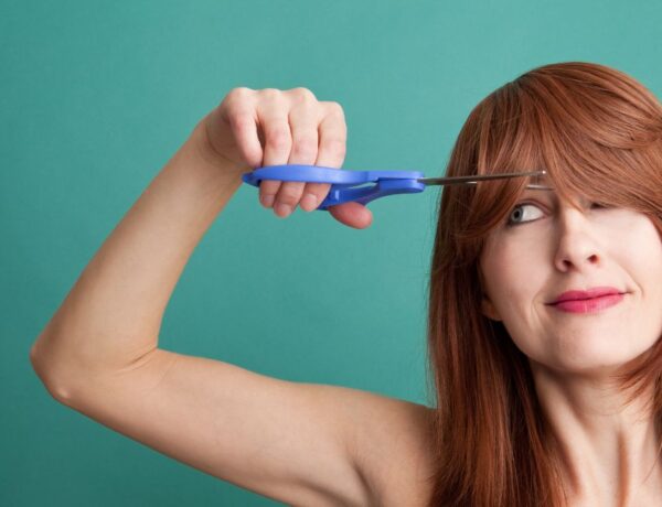 Femme coupant sa frange avec une paire de ciseaux bleus, illustrant une méthode de coupe de cheveux à domicile.